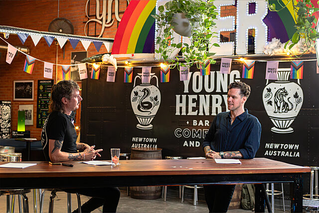 Two people sitting at a table in Young Henrys bar with skull illustrations, rainbow flags and bunting in the background.