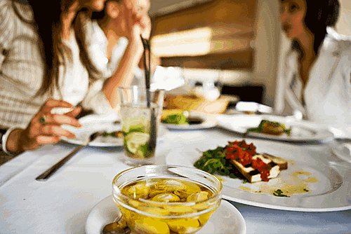 Dining table with plates of soup, salad, and an entrée, surrounded by three people with drinks.