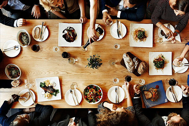 Top-down view of a dining table with people sharing a meal, featuring assorted dishes and drinks.