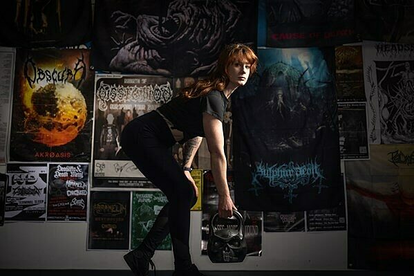 Elissa Jewell lifting a kettlebell in a dimly lit room with posters on the wall.
