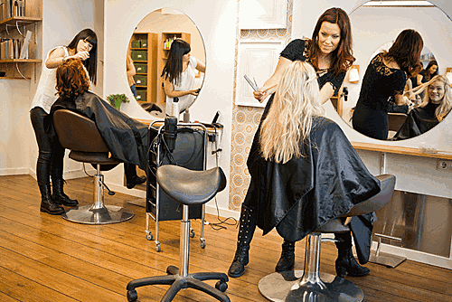 Hair salon with two hairstylists working on clients seated in front of large round mirrors.