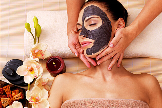 Person receiving a facial massage on a spa bed, surrounded by flowers, a candle, and spa items.