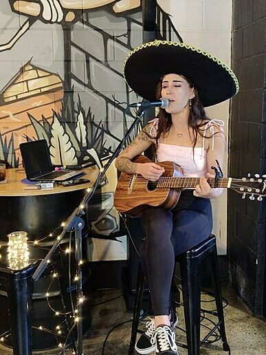 Guitarist in sombrero performing at Caffeine Kings with string lights and mural backdrop.
