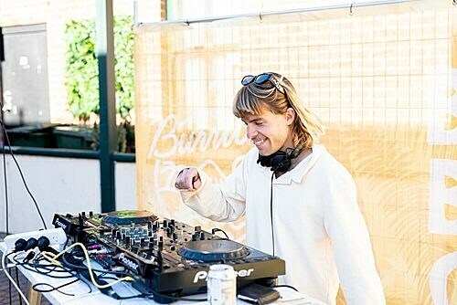 DJ behind turntables at Beach Burrito with headphones and drink can on table.