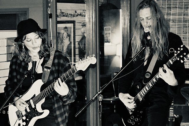 Two guitarists performing live at Banshees Bar, standing in front of microphones