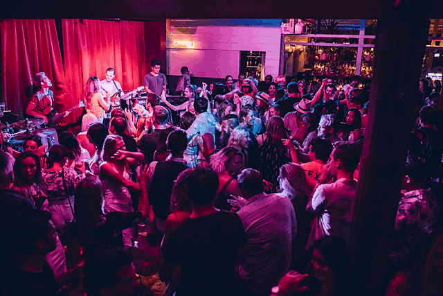 Live band performing on stage at The Sheaf with a packed audience and red-purple lighting.