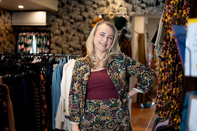 Caitlin standing inside Ramjet store, wearing a patterned outfit with clothing racks in the background.