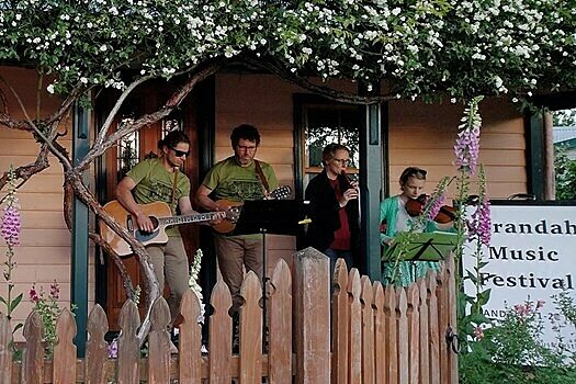 Musicians performing on a porch at the Verandah Music Festival, with greenery and flowers around.