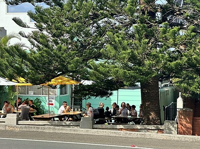 Outdoor seating area at Coledale RSL with people at picnic tables under trees and yellow umbrellas.