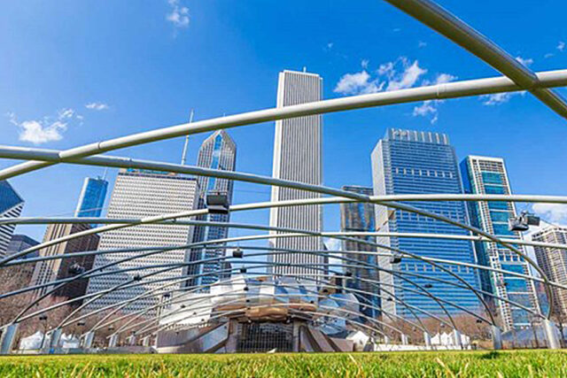 Chicago skyline with Willis Tower, metal pavilion structure, green grass, and clear blue sky.